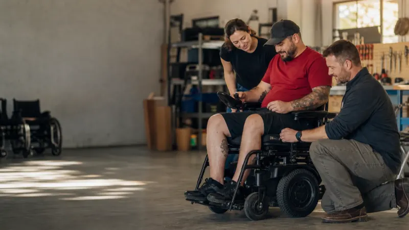 A wheelchair user and mobility equipment team working together on a power wheelchair.